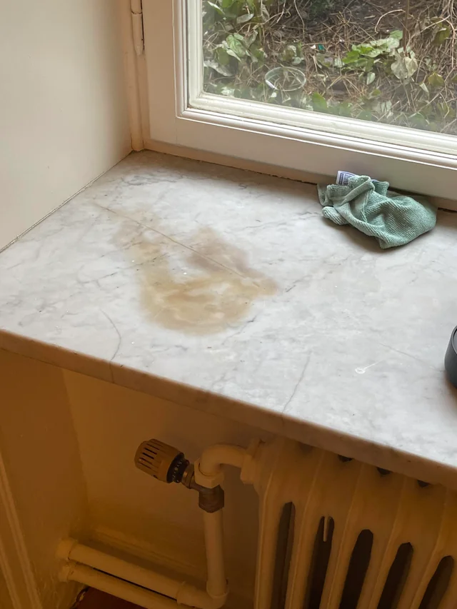 Mancha em pedra de mármore próxima à janela mostrando absorção de líquido